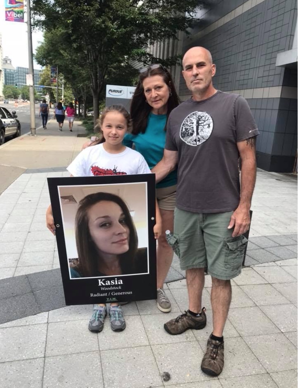 Caedence marches with her grandparents at Purdue Pharma in 2018, holding a photo of her mother.